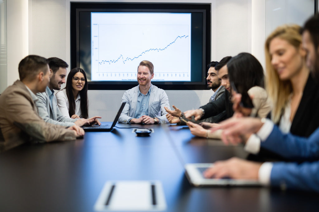 a group of people are sitting around a board room having a work meeting