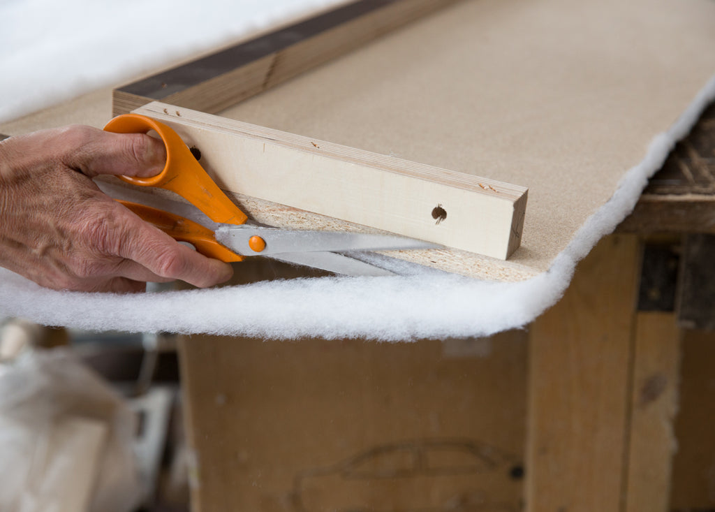 Excess fabric is being removed with a pair of scissors from a wooden frame